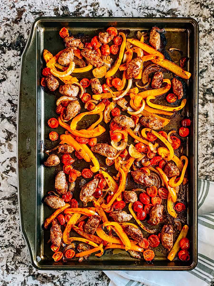 Freshly baked and delicious sausage and peppers on a rimmed baking sheet.