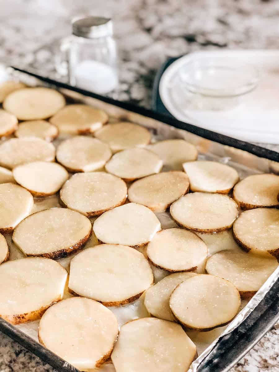 Tranches de pommes de terre côte à côte sur une plaque de cuisson tapissée de papier aluminium et recouverte de beurre fondu.