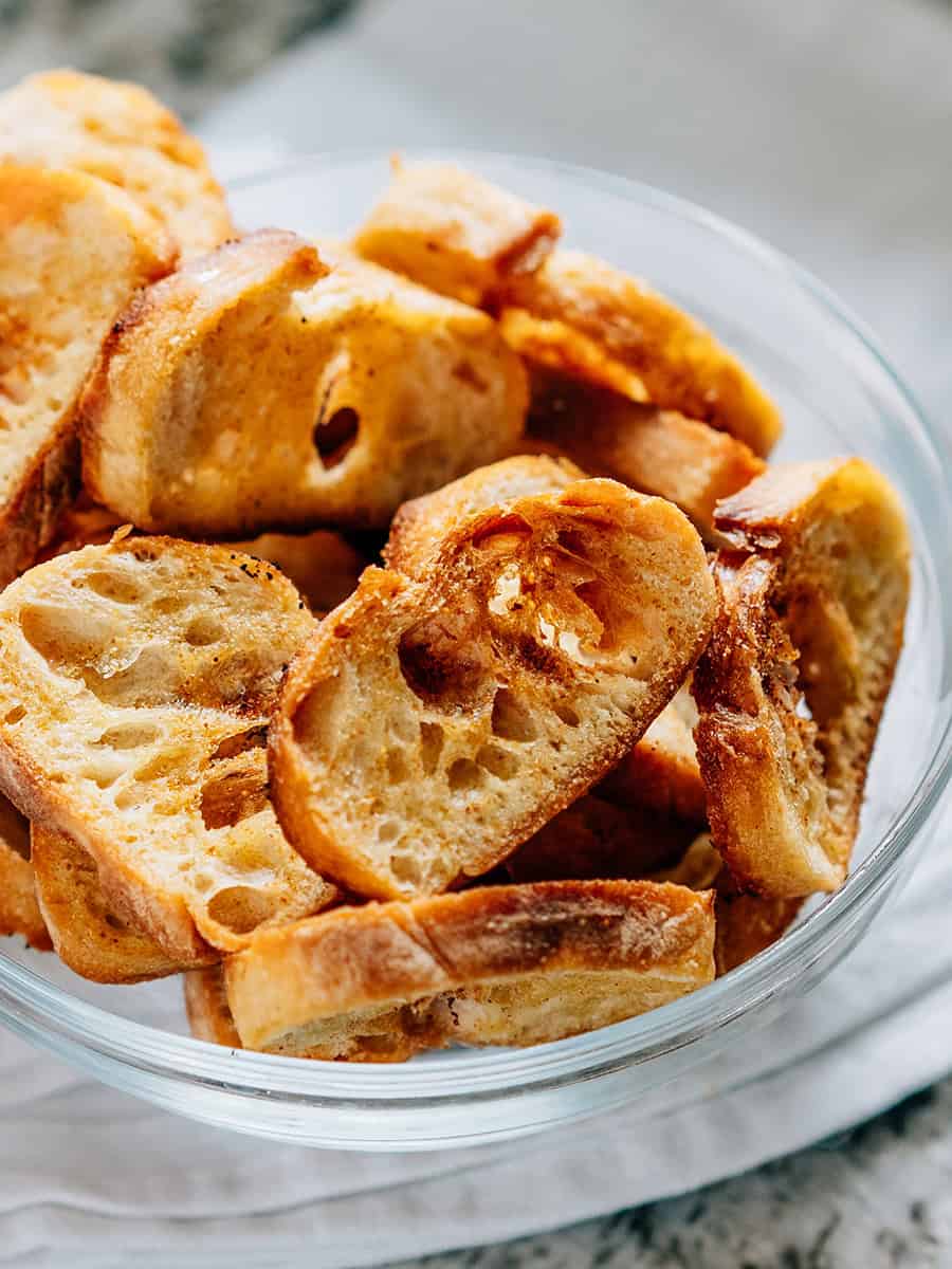 Vue latérale de tranches de baguette toastée à l'ail dans un bol en verre.