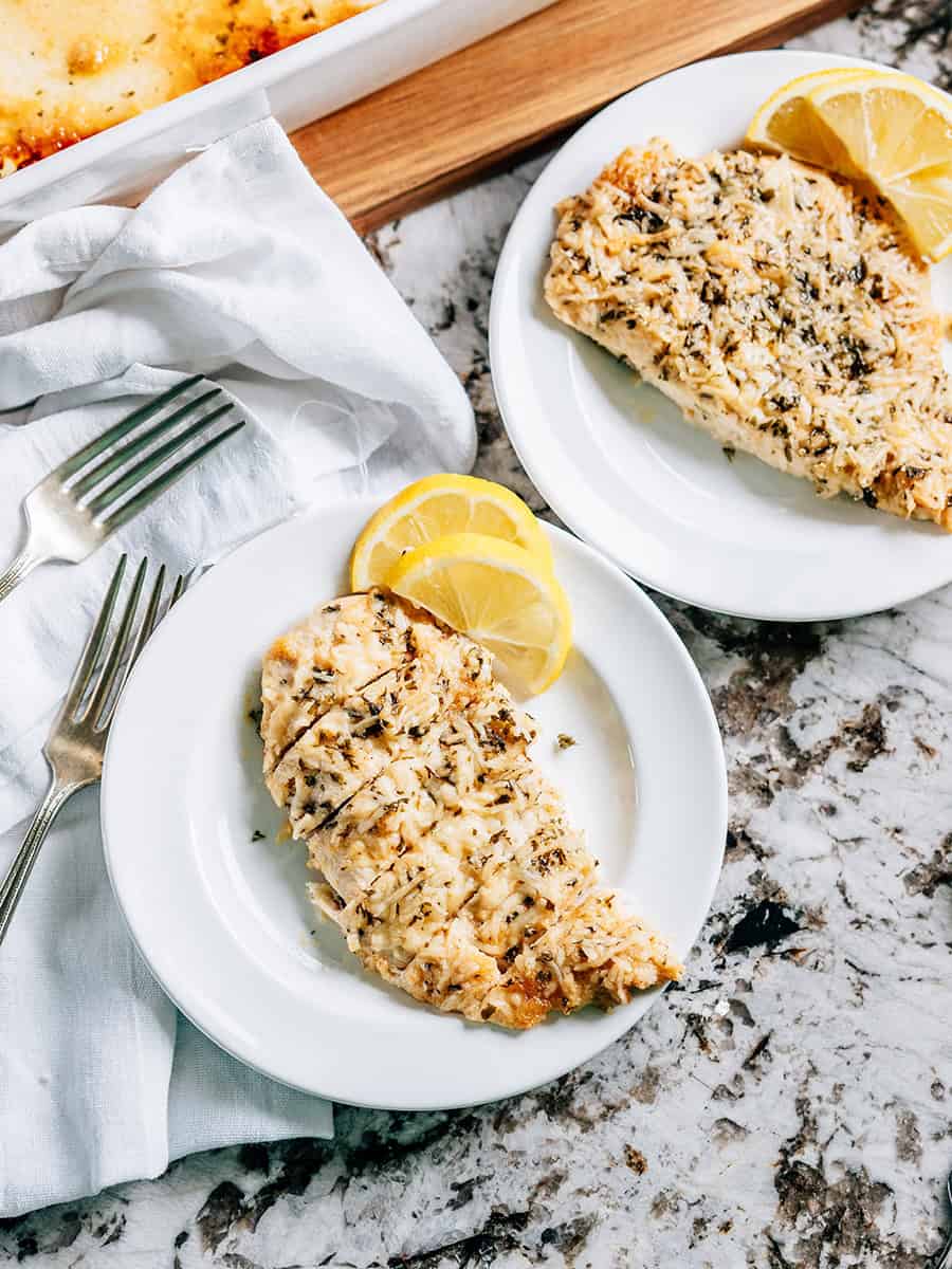 Un blanc de poulet au parmesan à l'ail tranché et servi avec des tranches de citron à côté.