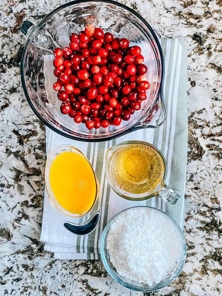 Ingredients for viral candid cranberries: Fresh cranberries in a bowl, 1 cup of 7-up pop, 1 cup of orange juice, and powdered sugar.