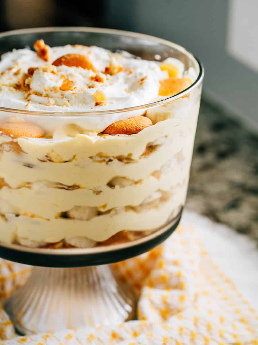 Couches de pudding à la vanille, de gaufrettes Nilla écrasées et de bananes tranchées dans un bol à trifle avec un nappage de crème fouettée.