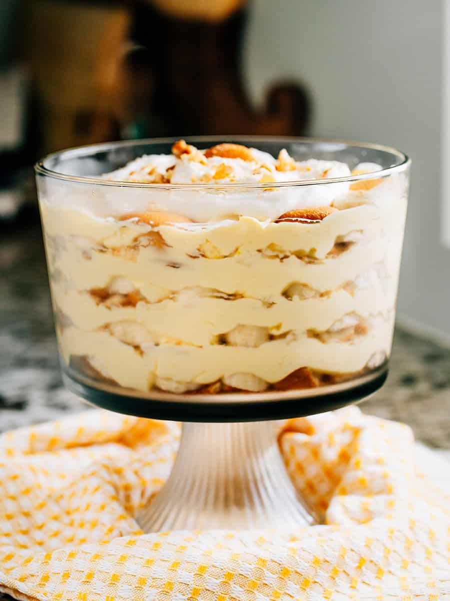 Couches de pudding à la vanille, de gaufrettes Nilla écrasées et de bananes tranchées dans un bol à trifle avec un nappage de crème fouettée. Ce dessert de pudding à la banane ravit tout le monde.