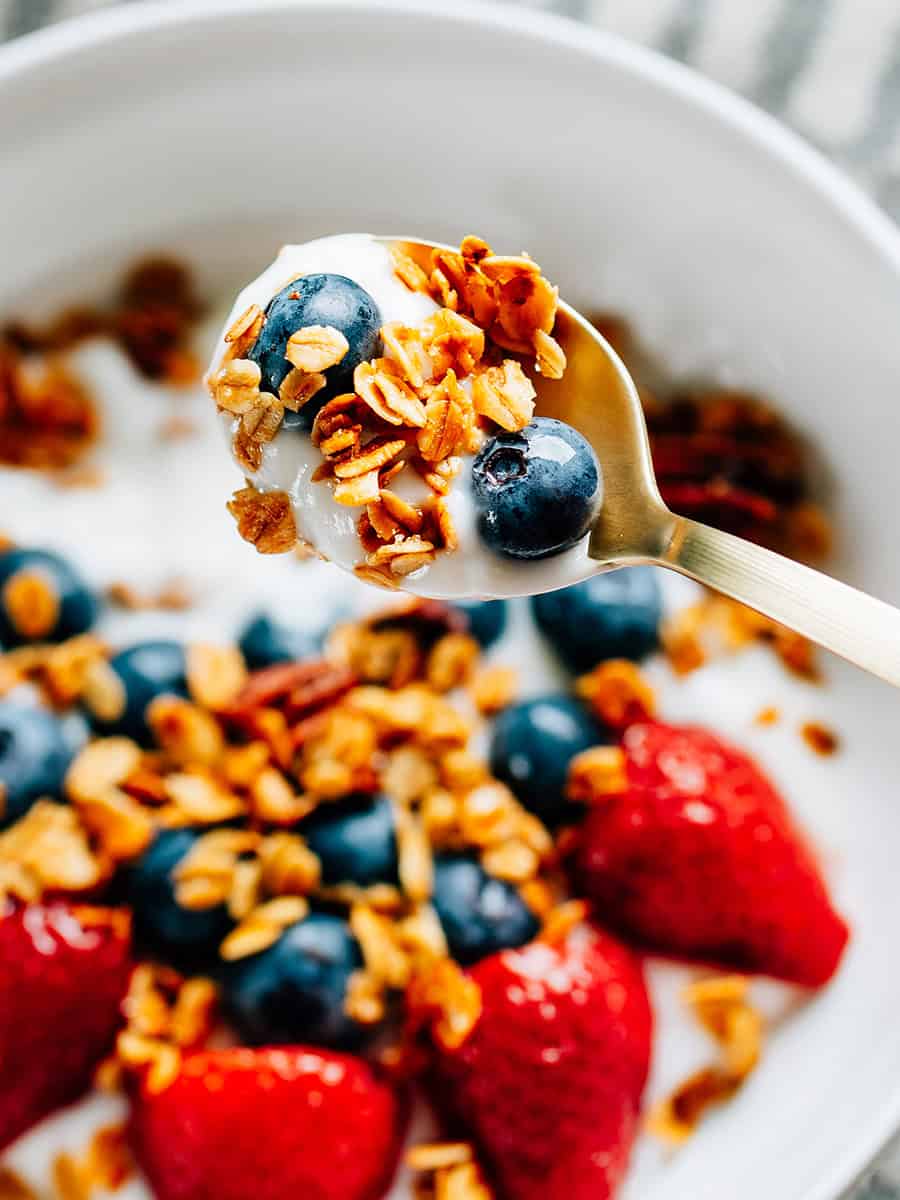 Une cuillère de granola au sucre et à la cannelle fait maison, des myrtilles fraîches et du yaourt, élevée au-dessus d'un bol pour une collation ou un petit-déjeuner coloré et savoureux.