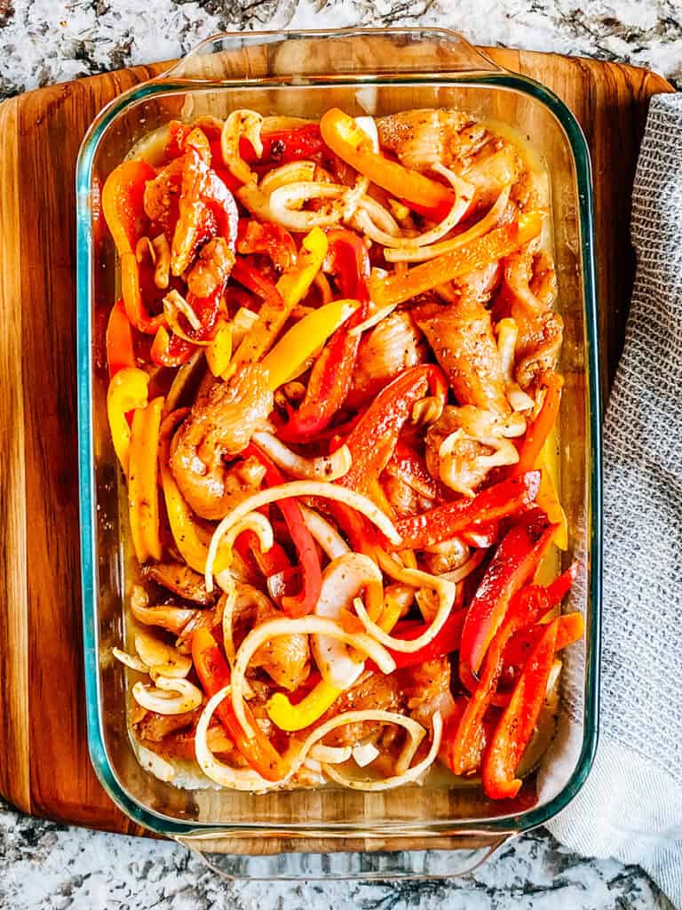 Le poulet et les poivrons assaisonnés dans un plat de cuisson de 23x33 cm sur le riz et le bouillon.
